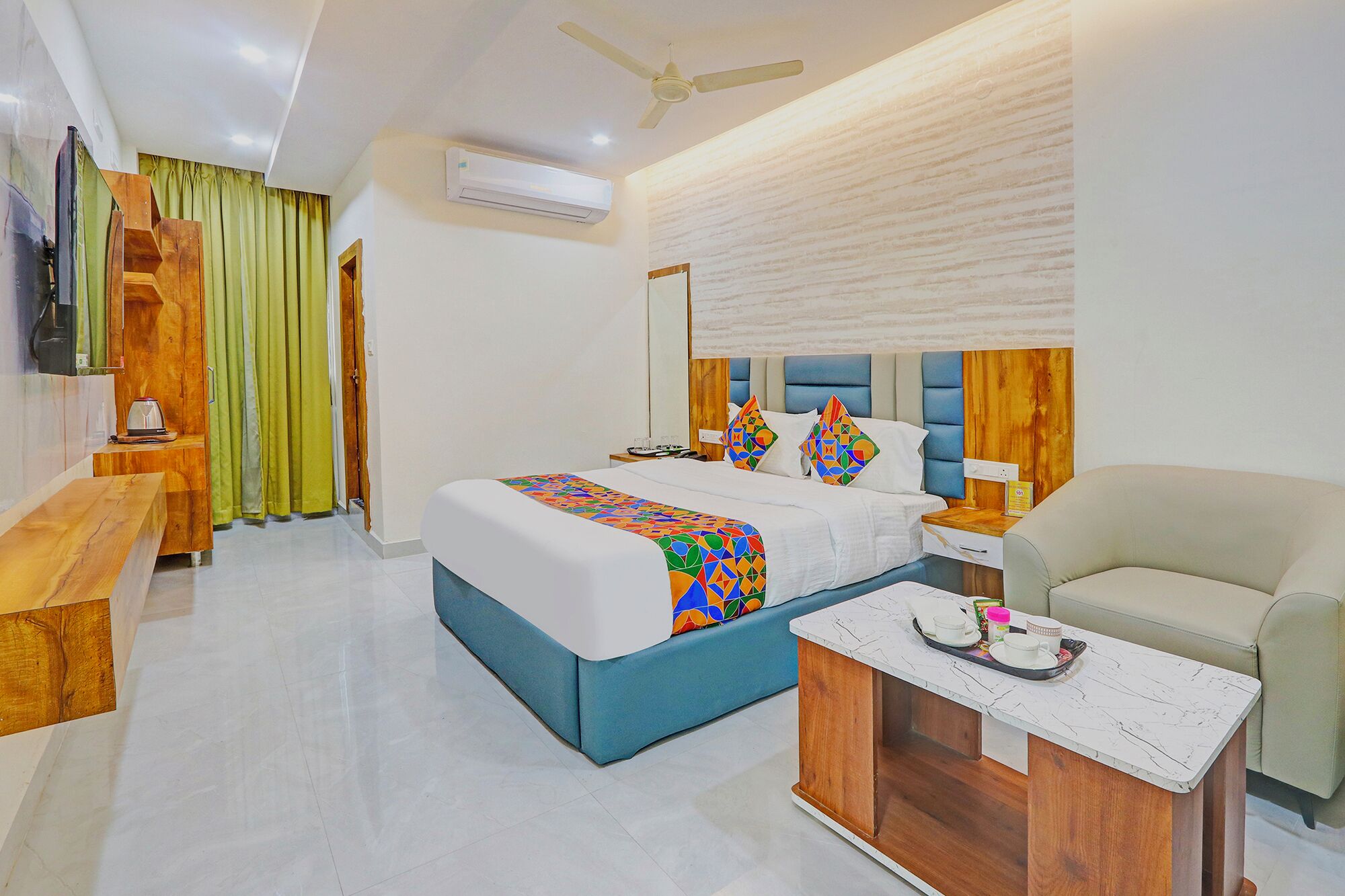 A hotel room with a bed, a wooden side table, a sofa, and a ceiling fan.