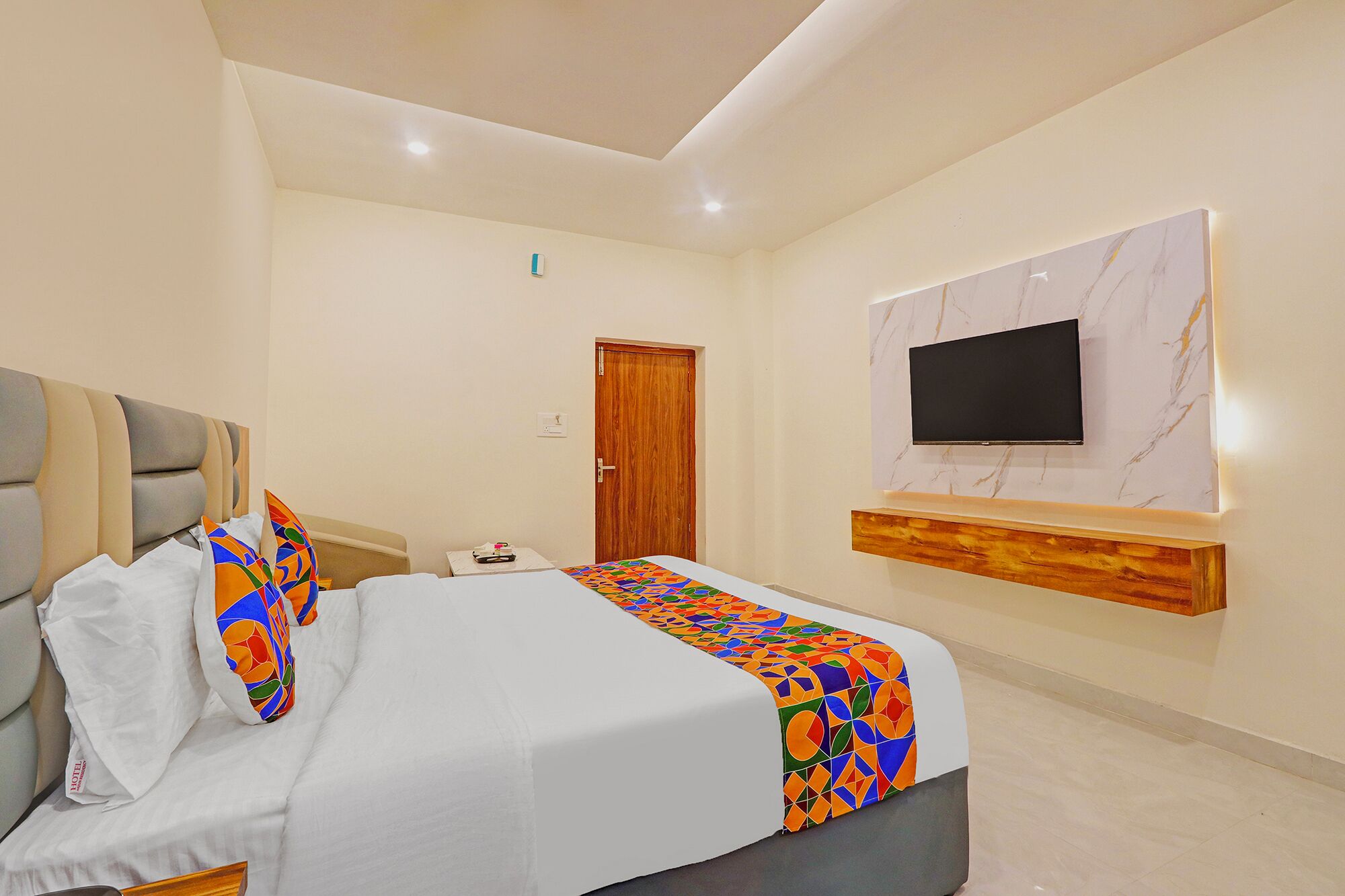 Una habitación de hotel con una cama, un televisor montado en la pared y una puerta de madera.