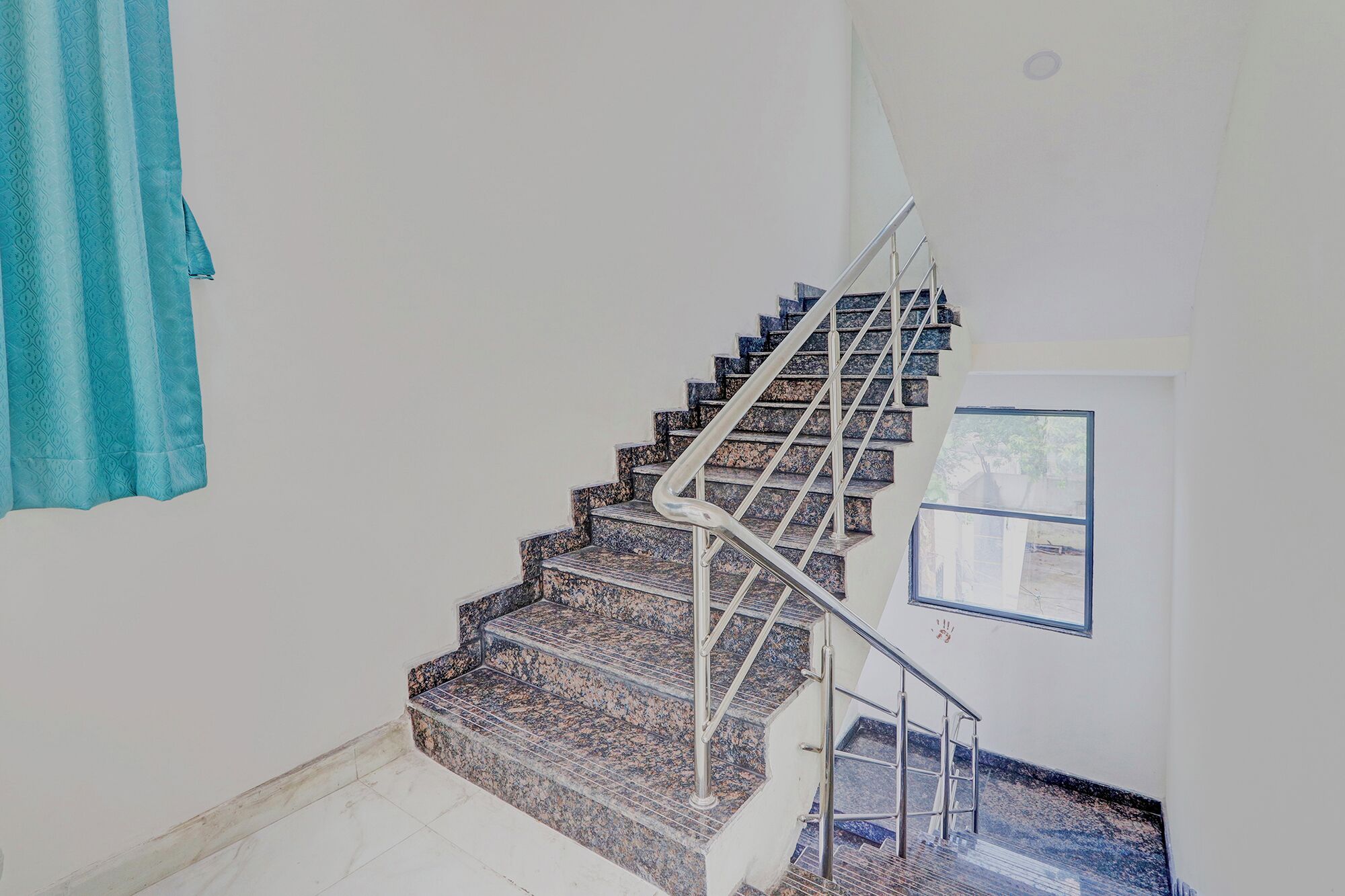 A staircase with a handrail, a window, and a towel hanging on the wall.