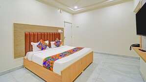 Un dormitorio moderno con cabecera de madera, cama con ropa de cama geométrica de colores, ventilador de techo y televisor de pantalla plana sobre un soporte de madera.