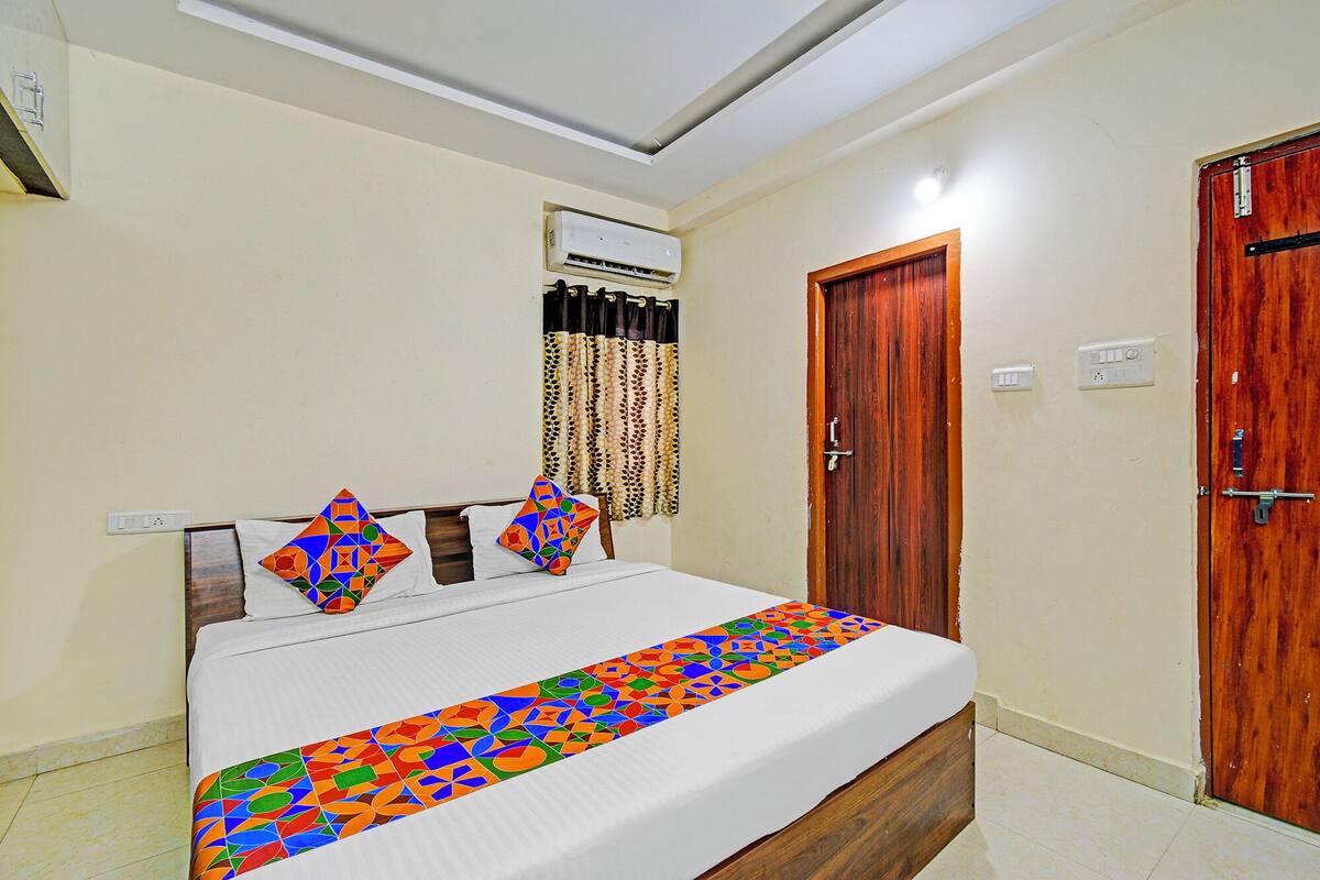 A bedroom with a bed, a wooden door, an air conditioning unit, and a wall-mounted light fixture.