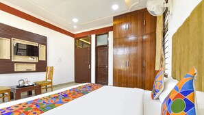 Quarto de hotel com cama, escrivaninha com cadeira, televisão e guarda-roupa.