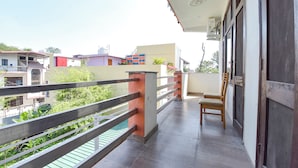 Uma varanda com grade de metal, uma cadeira de madeira e vista para edifícios vizinhos.