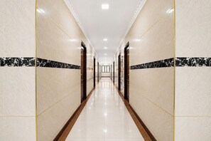A long, well-lit hallway with marble walls and a glossy floor, leading to a series of doors. - FabHotel Le Royal Inn (Chennai)