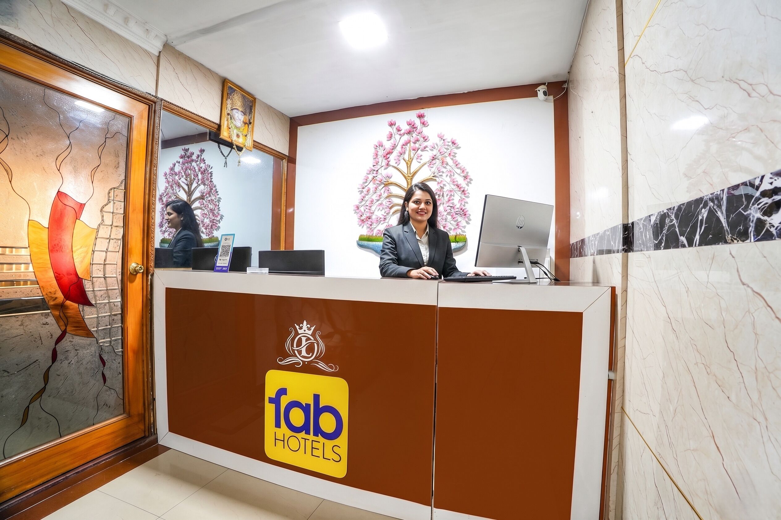 En receptionsdisk med 'fab hotels'-logo, en computer og et dekorativt træmaleri.