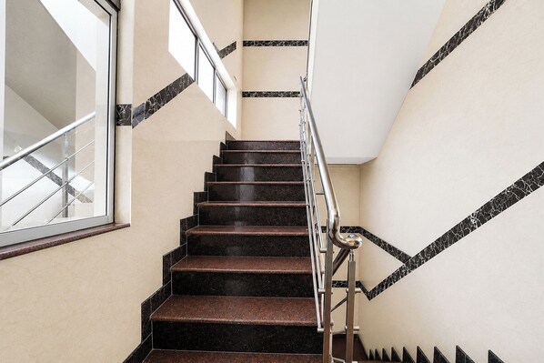 Un escalier avec des marches en marbre noir et une rampe en métal, menant à un palier doté d’une fenêtre.