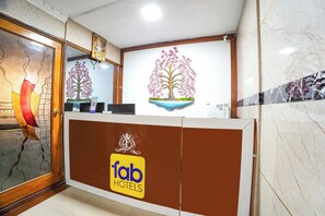A reception desk with a logo, a decorative tree mural, and a mirror. - FabHotel Le Royal Inn (Chennai)