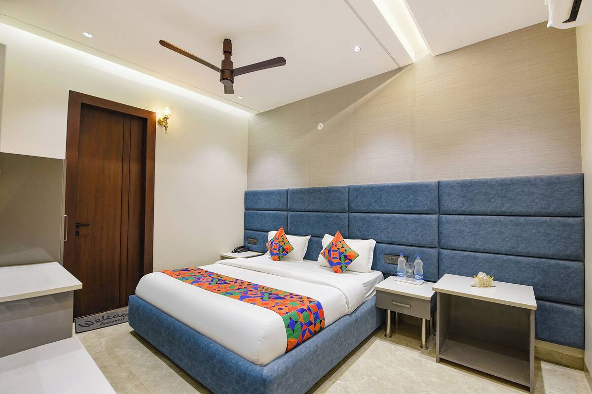 Una habitación de hotel moderna con una cama grande, un cabecero azul, una mesita de noche con lámpara y un ventilador de techo.