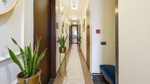 A hotel hallway with a patterned carpet, potted plants, framed pictures on the walls, and a bench on the right. - Fabhotel K9 Pearl (Ludhiana)