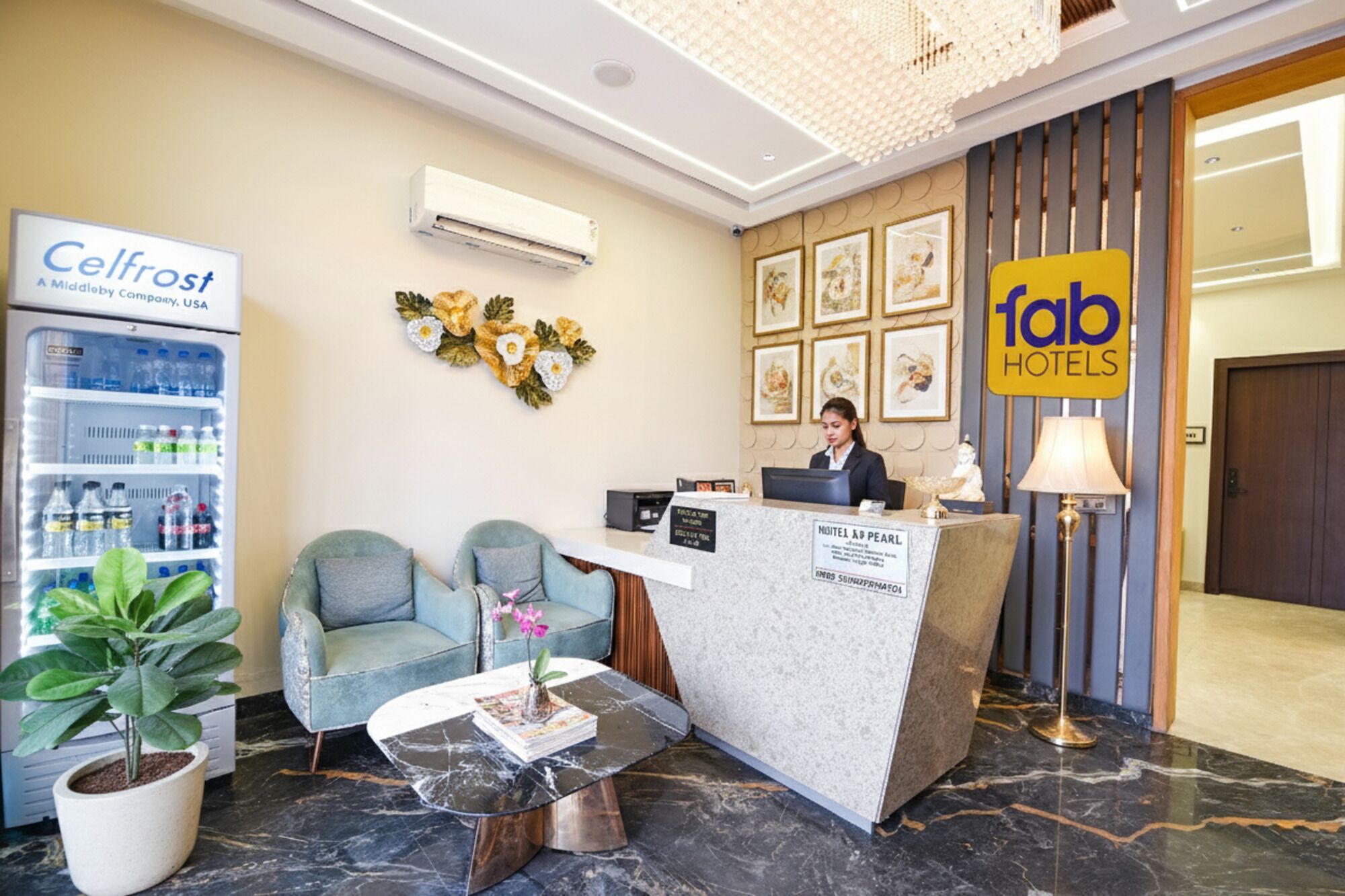 A hotel reception area with a reception desk, two armchairs, a coffee table, a refrigerator stocked with beverages, and a sign for 'Fab Hotels'.