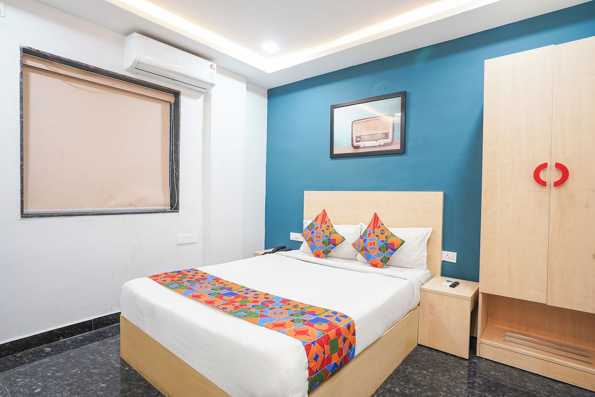 Habitación de hotel con cama, mesita de noche, armario y ventana con persianas.
