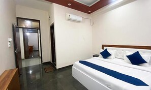 Quarto de hotel com cama, mesa de cabeceira, espelho e porta que dá para outro cômodo.