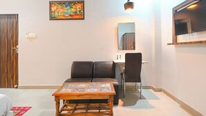 A modern living room with a sofa, a coffee table, a dining table with chairs, a painting on the wall, and a TV mounted on the wall. - Fabhotel Sr Grand (Lucknow)