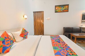A hotel room with a bed, a sofa, a wooden door, and a painting on the wall.