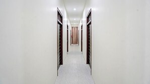 Un pasillo estrecho y bien iluminado con paredes blancas y suelo de baldosas, que conduce a una habitación con una puerta estampada.