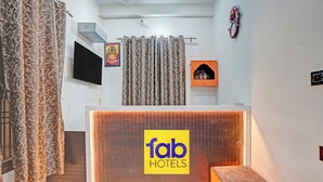Zona de recepción de un hotel con un cartel de 'fab hotels', un televisor, un reloj y un pequeño santuario.