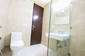 A bathroom with a toilet, a glass shower enclosure, and a sink with a mirror above it. - Fabhotel Am Bliss (Gurugram)