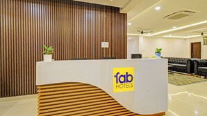A reception desk with a logo, a wooden slatted wall, a sofa, and a ceiling fan. - Fabhotel Dolce Vita Grand (Hyderabad)