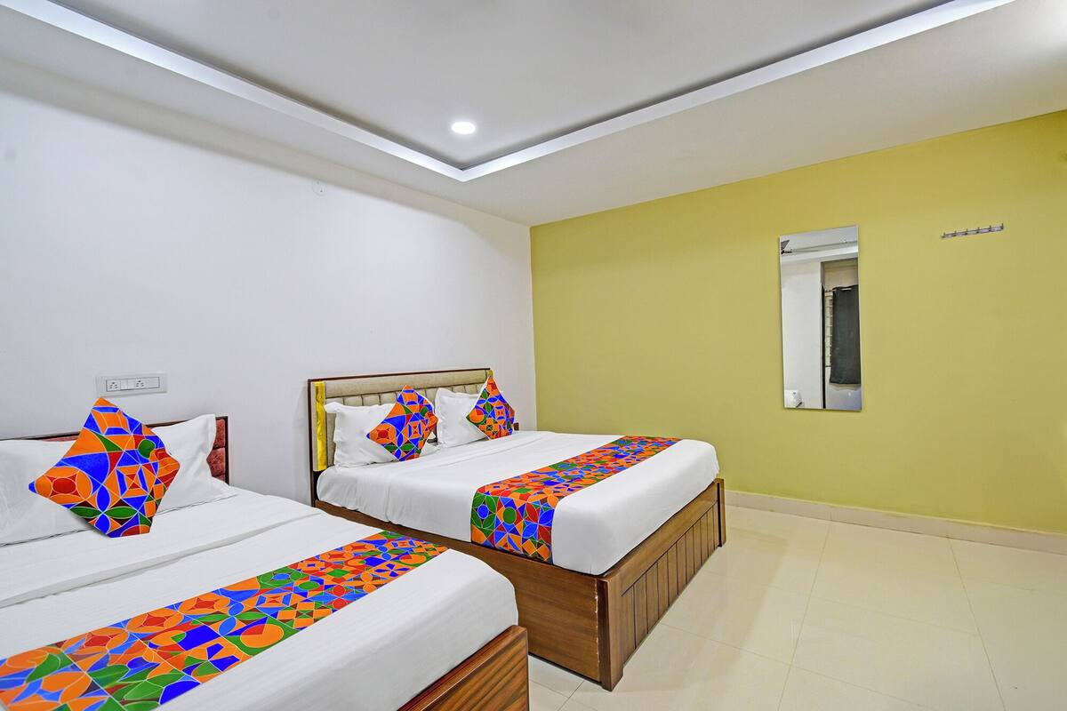 A hotel room with two beds, a mirror, and a yellow wall.