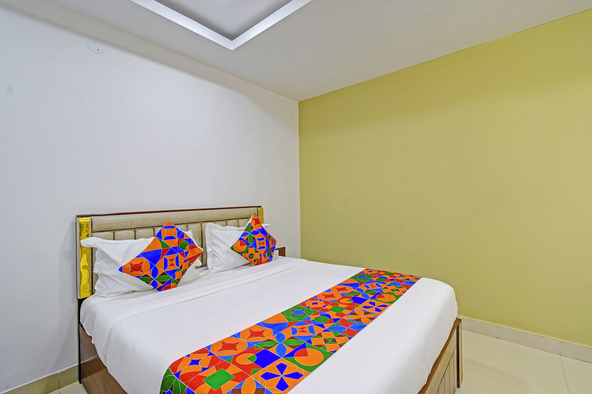 A bed with a white mattress and colorful geometric-patterned bedspread.