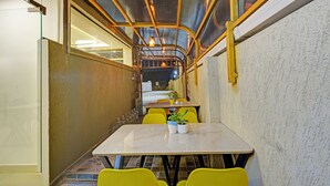 An indoor dining area with a long table and yellow chairs, a glass wall on one side, and a metal ceiling structure. - Fabhotel Dolce Vita Grand (Hyderabad)