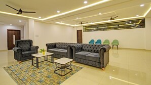 A modern living room with a sectional sofa, two armchairs, a coffee table, and a patterned rug. There are ceiling fans, recessed lighting, and a large window with a view. - Fabhotel Dolce Vita Grand (Hyderabad)