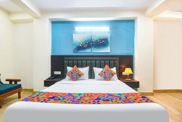 Habitación de hotel con una cama grande, una mesita de noche, una lámpara y una pared azul con un cuadro.