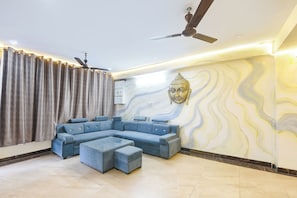 Una sala de estar moderna con un sofá modular, una mesa de centro, un ventilador de techo y una pared decorada con una escultura de Buda.