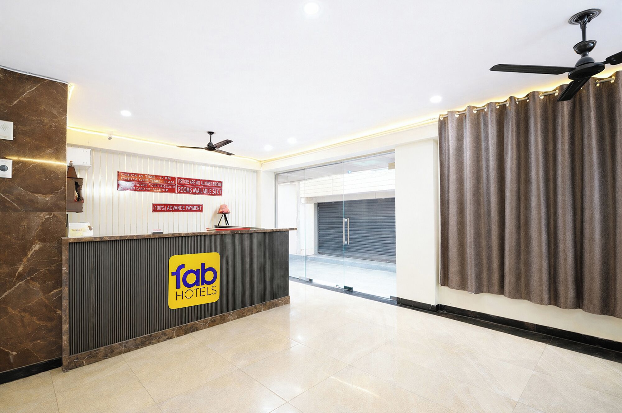 A hotel reception area with a check-in counter, a ceiling fan, and a view of the outside.