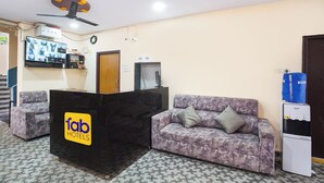 A reception area with a reception desk, a sofa, a ceiling fan, a television, and a water dispenser. - Fabhotel Sbr (Hyderabad)