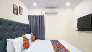 A hotel room with a tufted headboard, a bed with white bedding and a colorful geometric throw, a dark curtain, an air conditioning unit, and a mounted television. - Fabhotel Sbr (Hyderabad)
