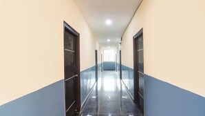 A long, narrow hallway with doors on both sides, leading to a bright room at the end. - Fabhotel Sbr (Hyderabad)