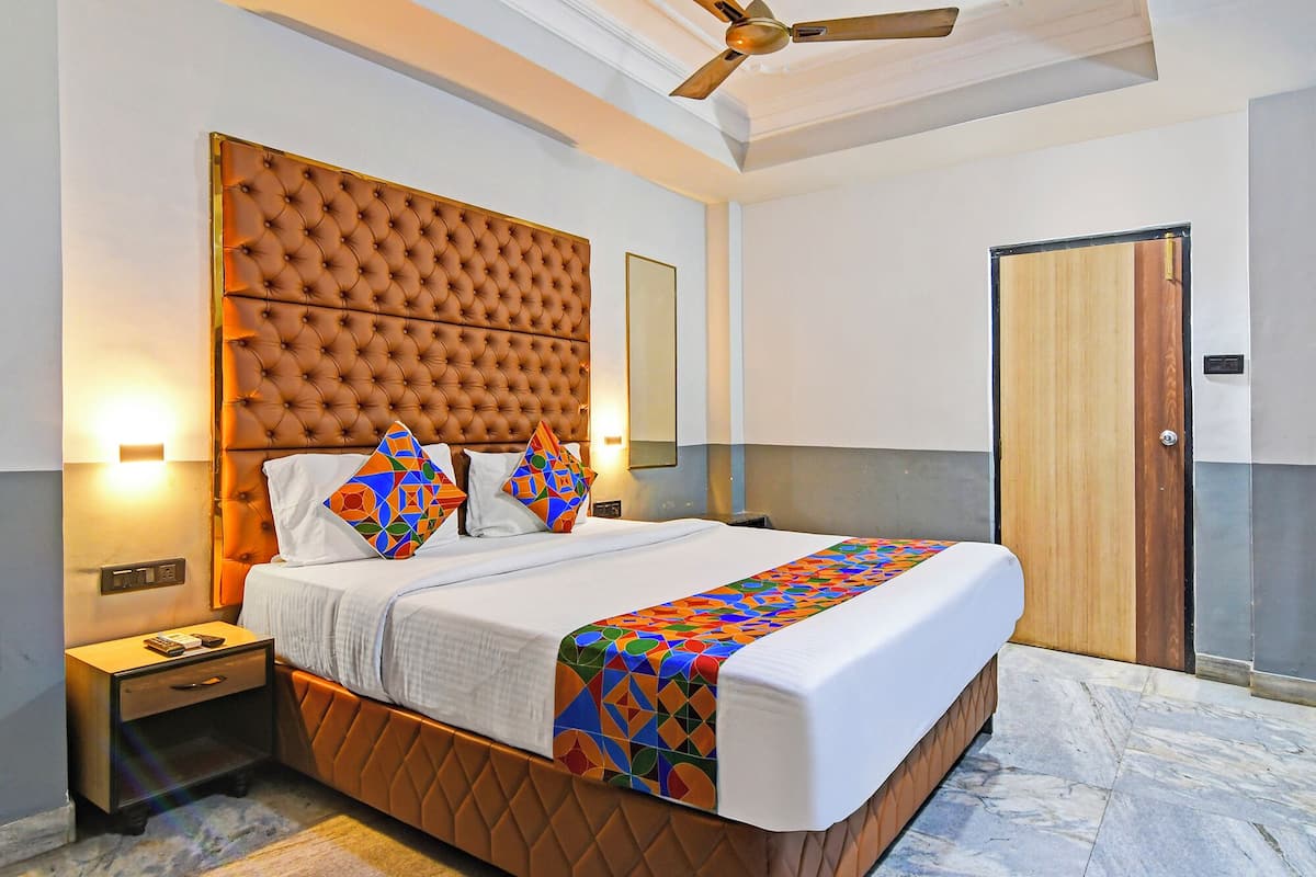 Une chambre à coucher avec une tête de lit capitonnée, un lit agrémenté de coussins géométriques aux couleurs vives, une table de chevet avec une lampe et un ventilateur de plafond.