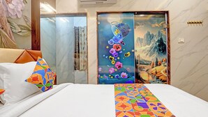 Una habitación de hotel con una cama, una colcha colorida, un cuadro de flores y montañas en la puerta, y vistas a las montañas desde la ventana.