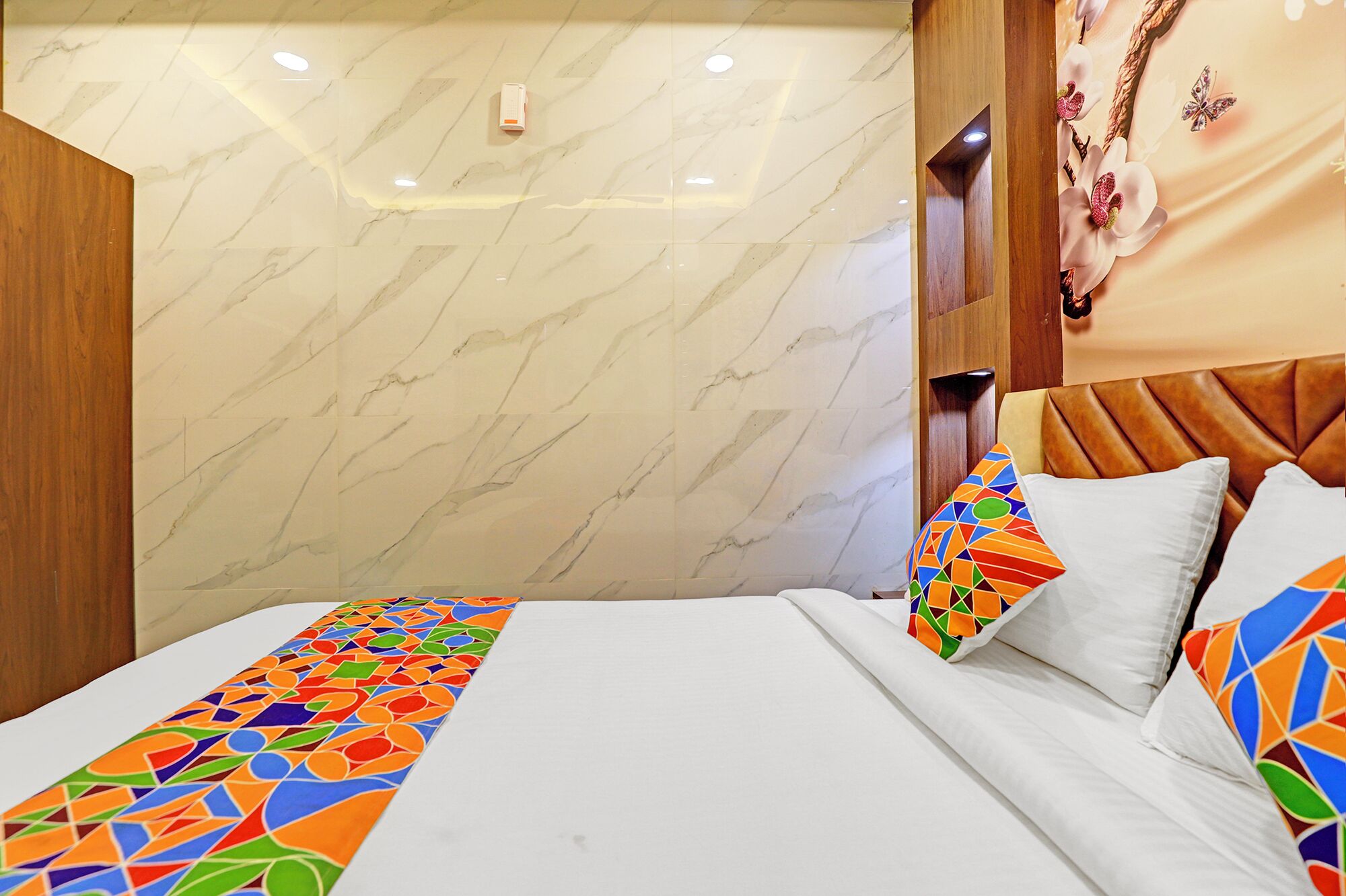 A hotel room with a marble wall, a wooden headboard, and a bed with colorful geometric pillows.