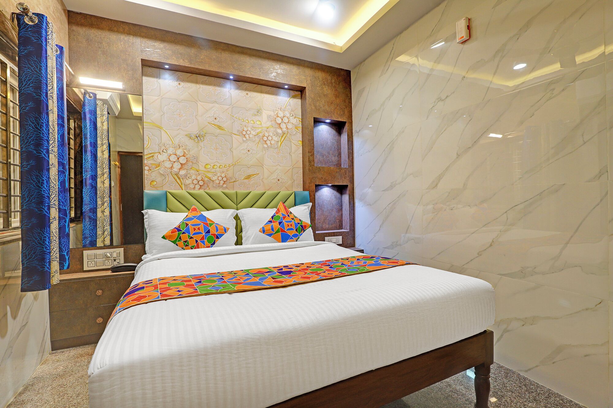 Habitación de hotel con una cama grande, cabecero tapizado en verde y un panel decorativo en la pared.