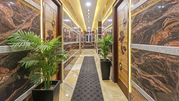 Un pasillo con paredes de mármol, plantas en macetas y una alfombra estampada que conduce a una puerta con un emblema de corona.