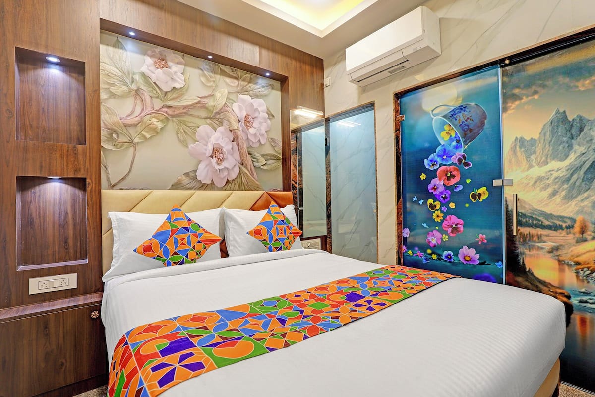 A hotel room with a bed, floral wallpaper, a large painting, and a wooden headboard.