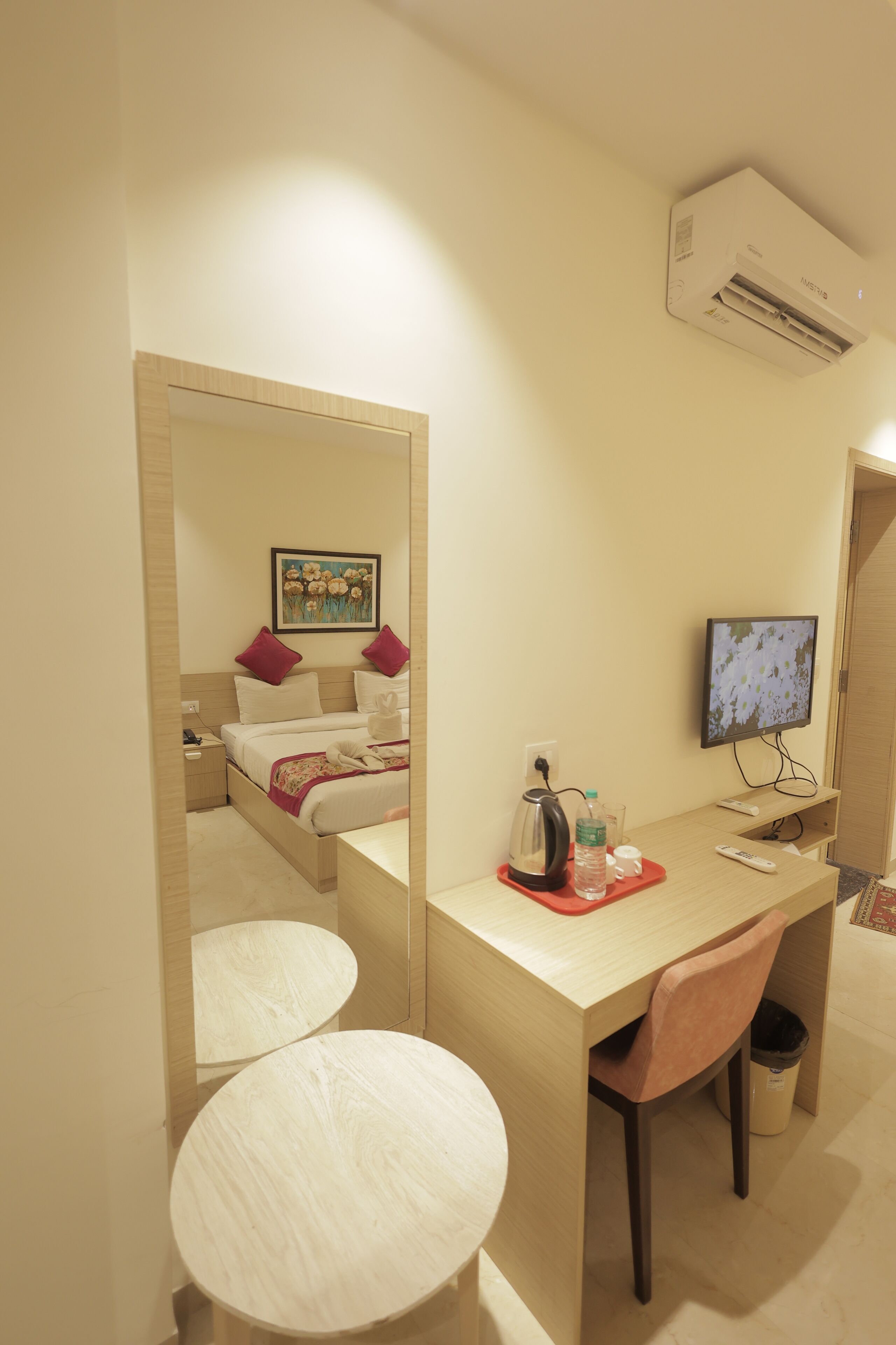 A hotel room with a bed, a desk with a chair, a TV, and a mirror.