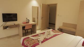 Quarto de hotel com cama, secretária, televisão e guarda-roupa.