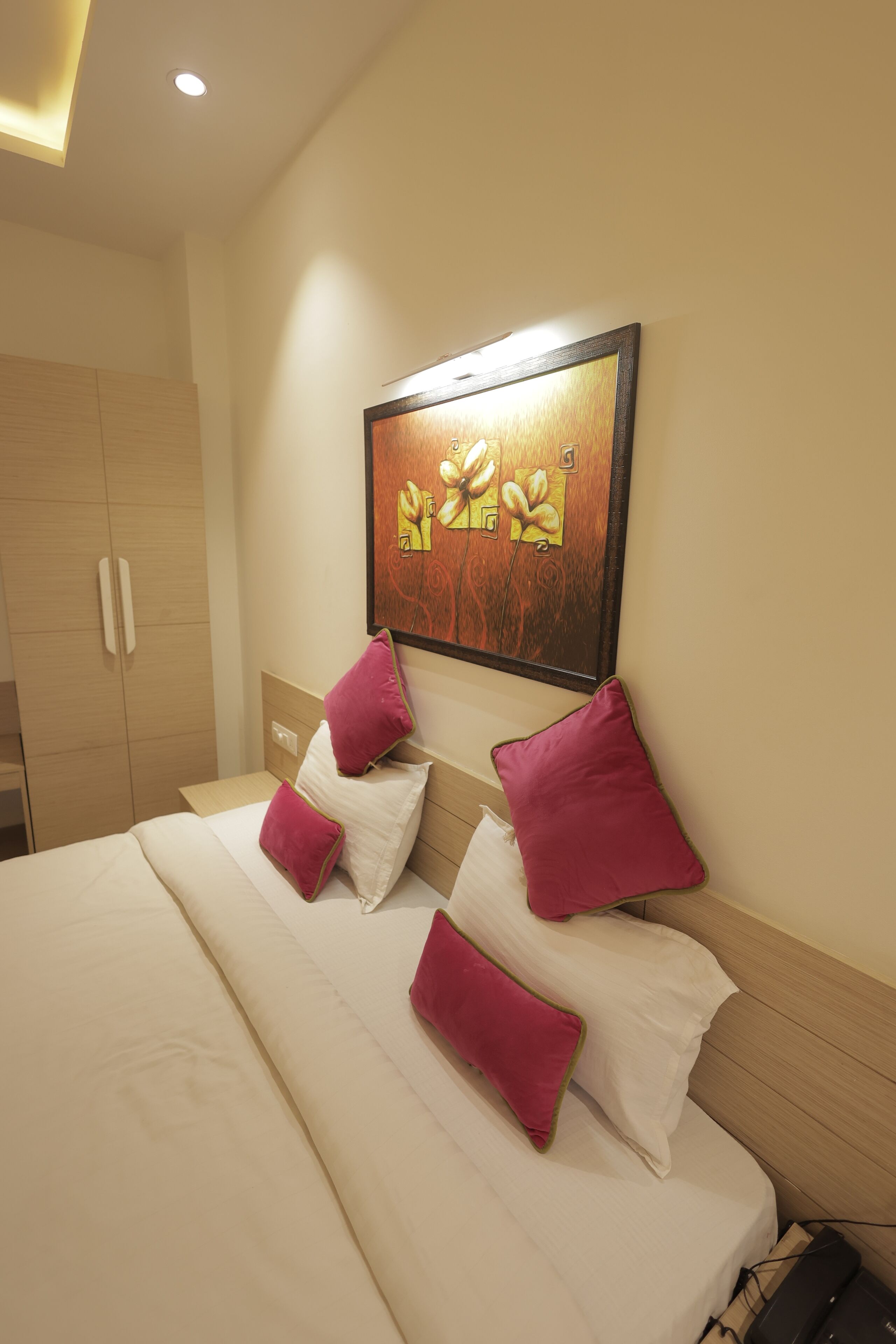 A hotel room with a bed, a wooden wardrobe, and a painting on the wall.