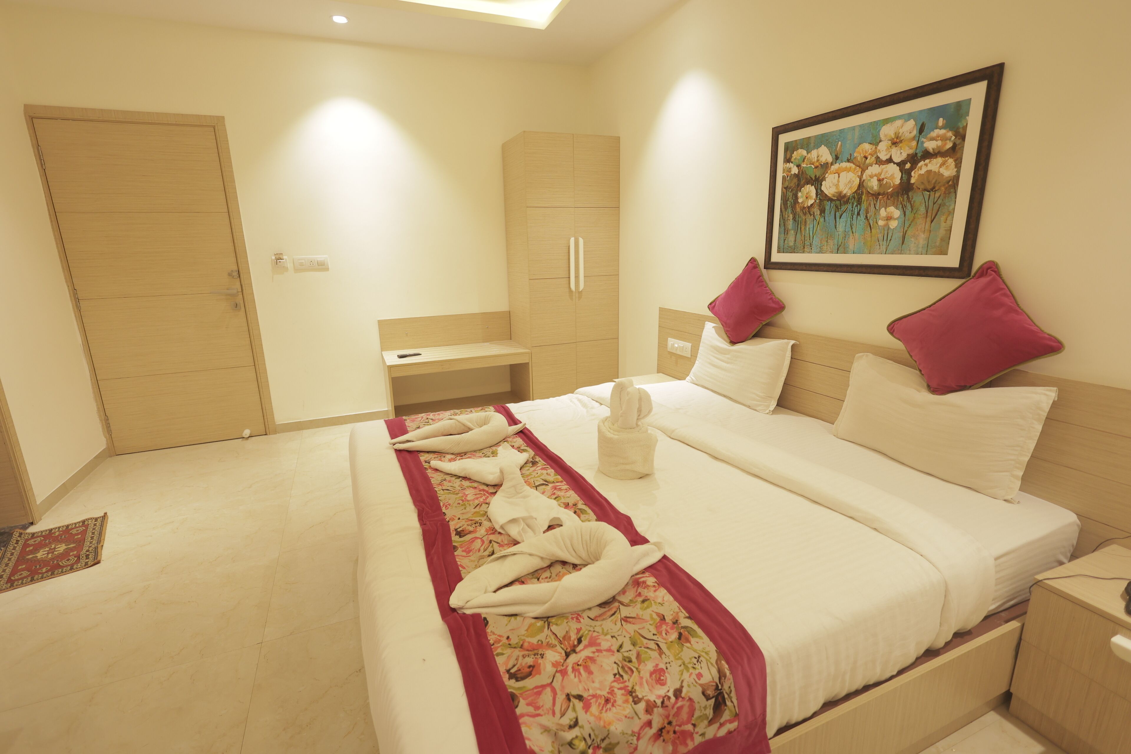 A hotel room with a bed, a desk, a wardrobe, and a painting on the wall.