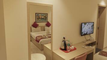 Habitación de hotel con cama, escritorio con silla, televisor y aire acondicionado.