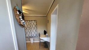 Kapea käytävä, jonka lattia on laatoitettu. Vasemmalla puolella on valkoinen ovi ja oikealla puolella ruskea ovi.