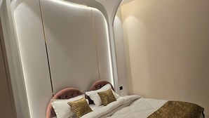 A modern bedroom with a curved ceiling, a bed with white bedding and gold accents, and a ceiling fan. - Hotel Parth (Faizabad)