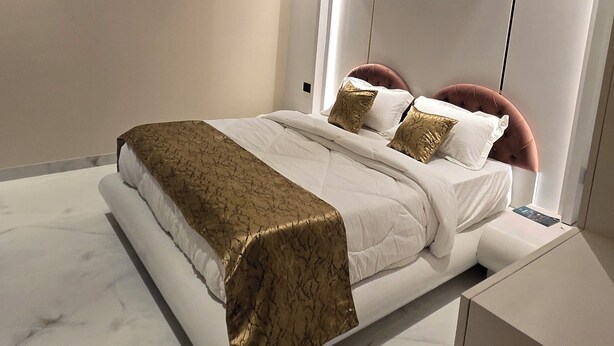 A modern bedroom with a curved ceiling, a bed with white bedding and gold accents, and a minimalist design. - Hotel Parth (Faizabad)