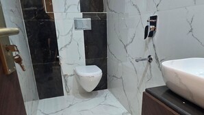 A modern bathroom with a marble floor, a white toilet, a sink with a mirror, and a dark wooden cabinet. - Hotel Parth (Faizabad)