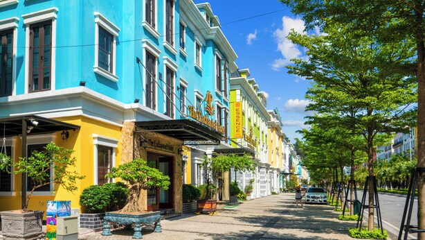 Une rangée de bâtiments aux couleurs vives, une rue pavée, des plantes en pot et un ciel bleu azur.