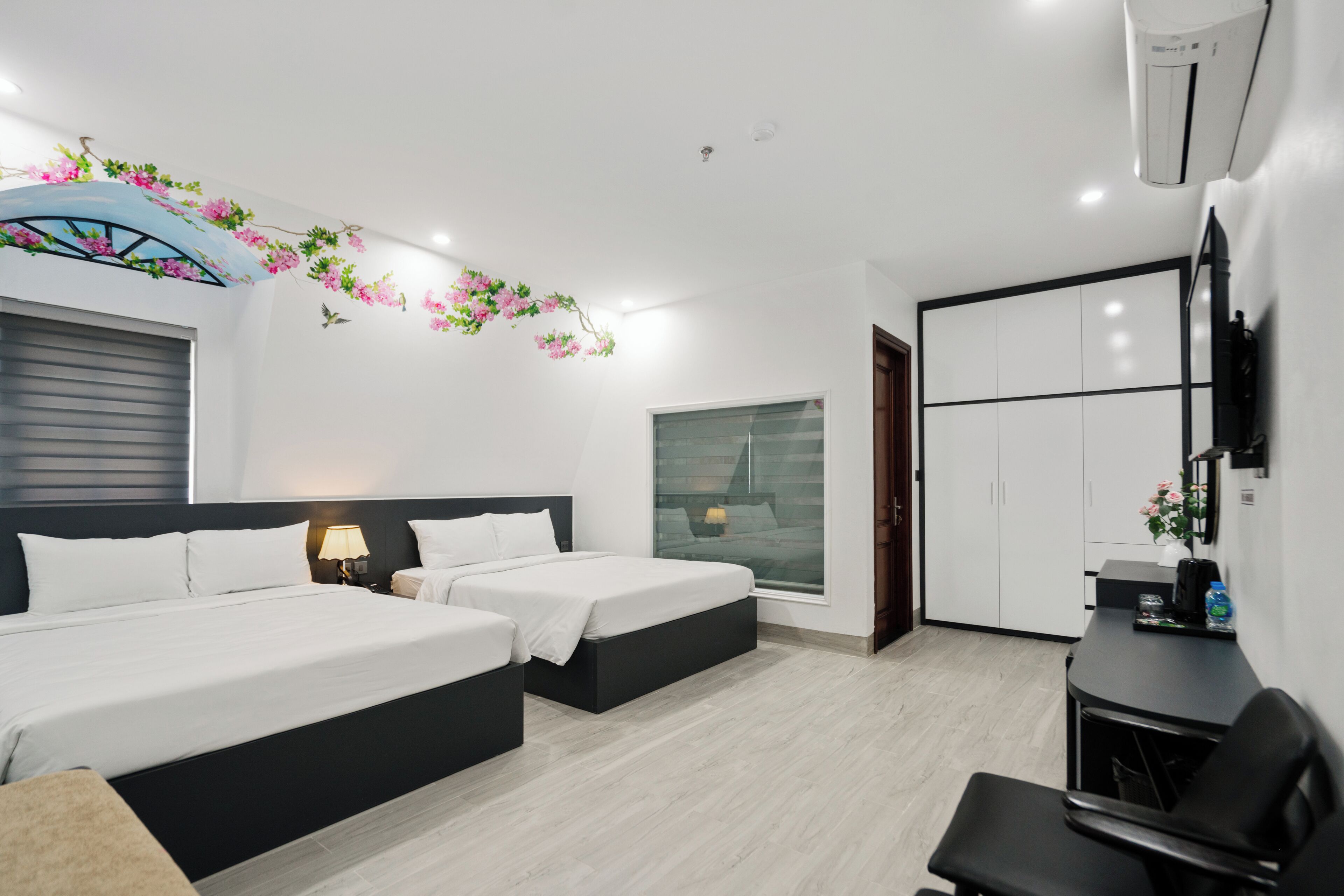 Quarto de hotel moderno com duas camas, uma escrivaninha, uma cadeira e um guarda-roupa.