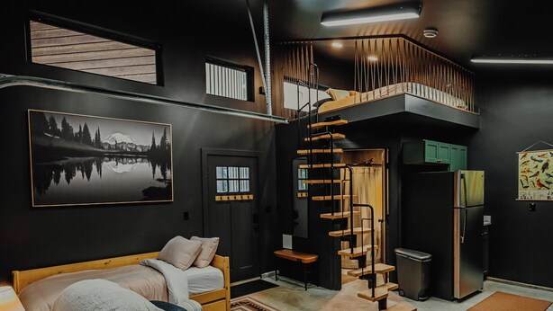 A modern living room with a wooden sofa, a staircase, and a large painting on the wall. - Modern Mountain Mini House- studio house w/ sleeping loft Packwood with WIFI, AC (Packwood)